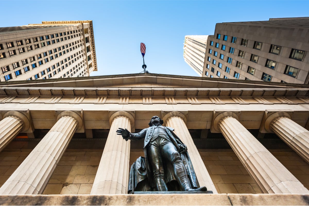 Statue in front of a columned institutional building with skyscrapers, representing the American financial and political system
