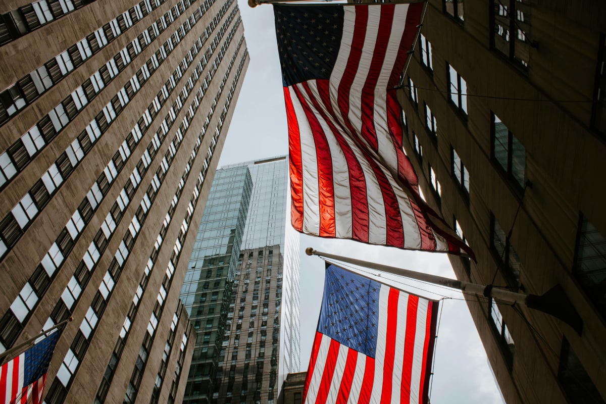 United States flags waving in front of skyscrapers in an urban street, illustrating the American economy and financial center