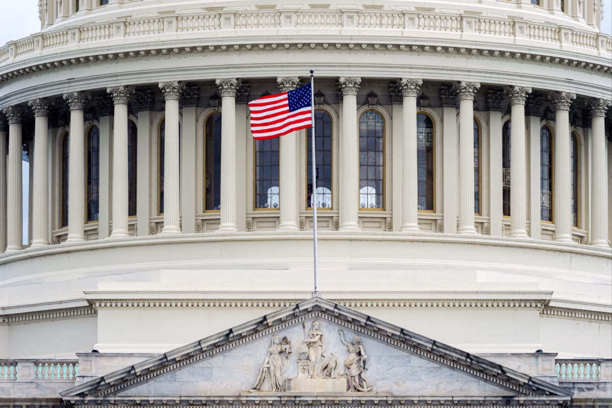 United States flag in front of a columned institutional building, symbolizing American politics and economy