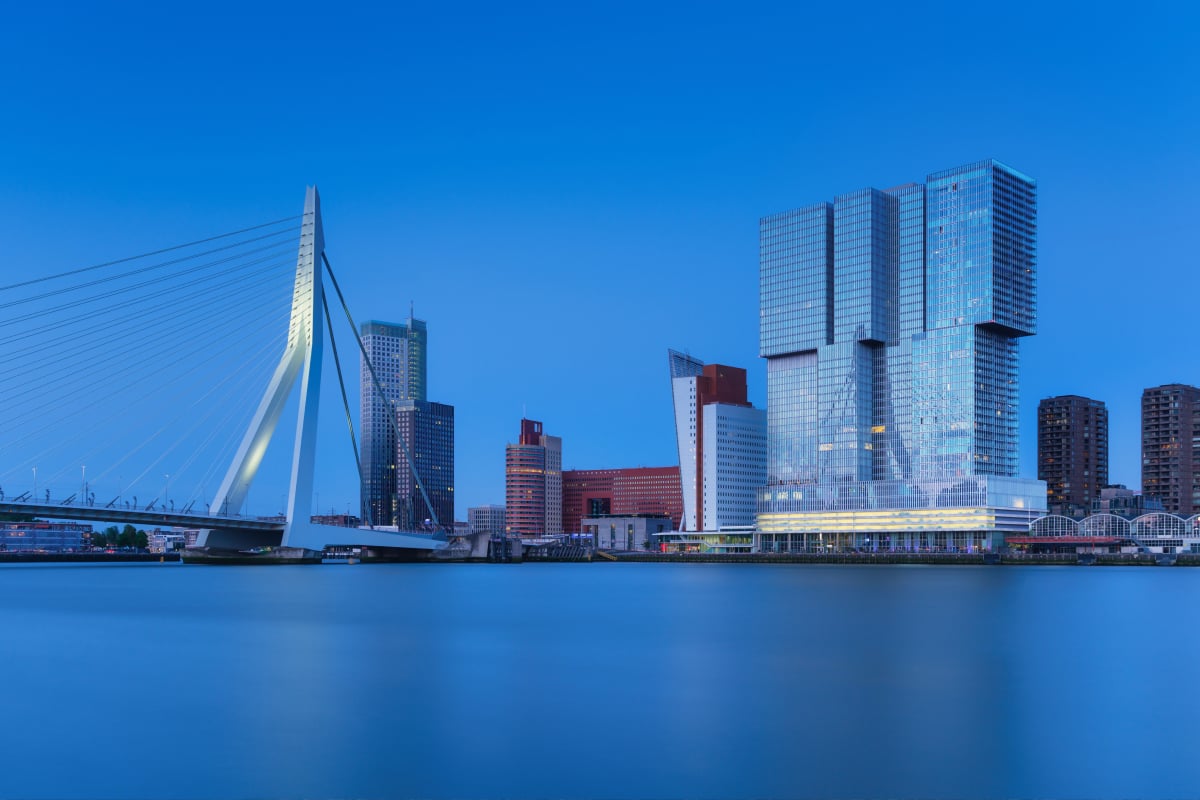 City skyline at dusk featuring modern high‑rise buildings and a cable‑stayed bridge spanning a river.


