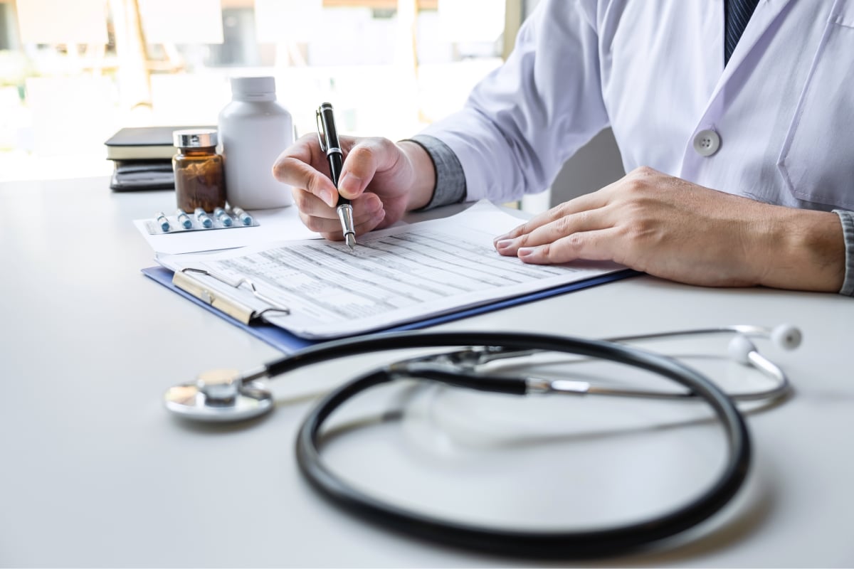Healthcare professional writing on a medical record with a stethoscope on the table, illustrating consultation and patient care
