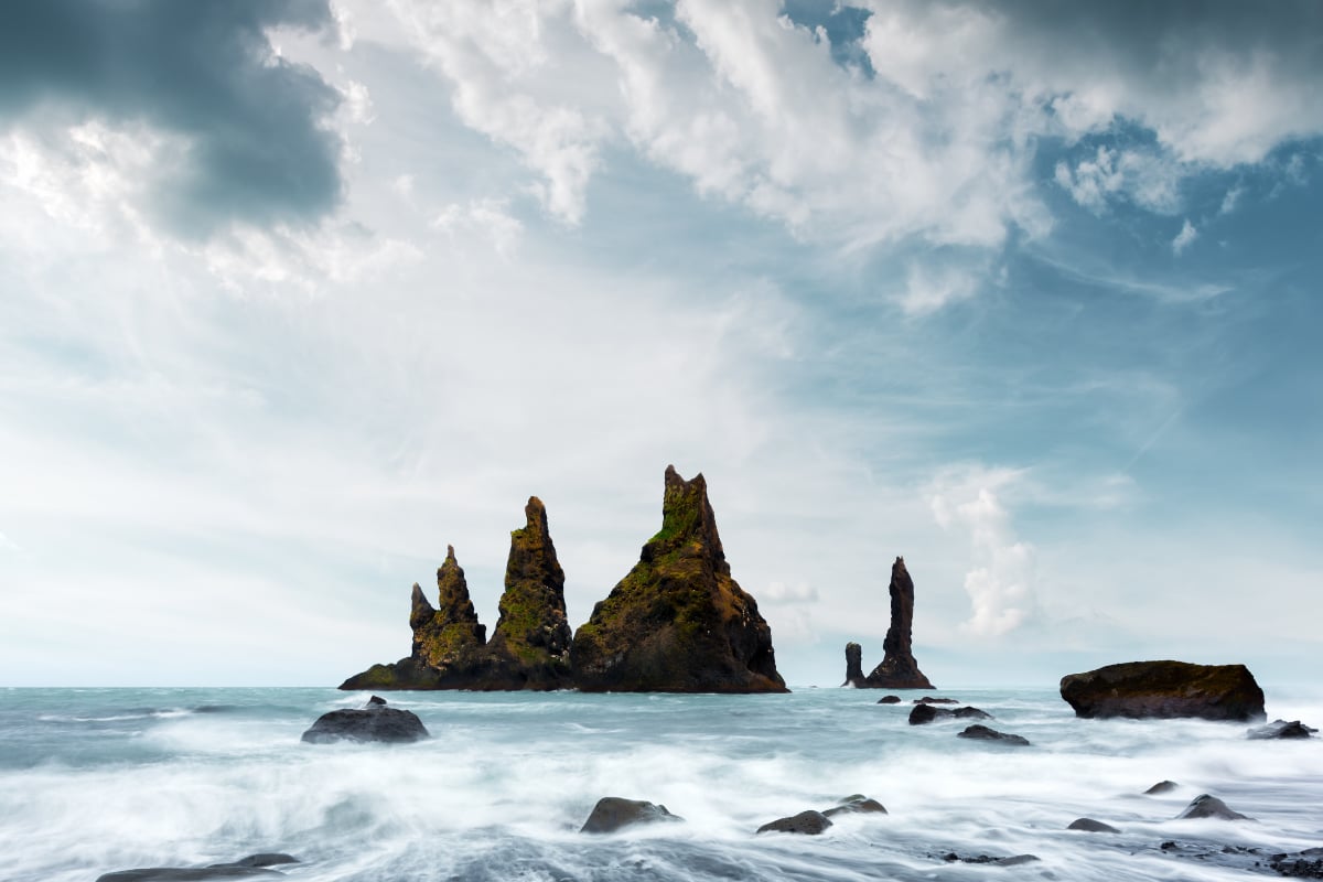 Volcanic rock formations rising from the ocean with waves and cloudy sky, illustrating a wild natural landscape and the power of nature
