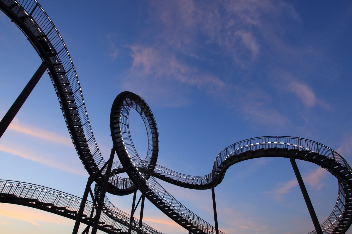 Elevated metal walkway forming loops and curved paths, supported by pillars, seen against a blue sky at dusk.

