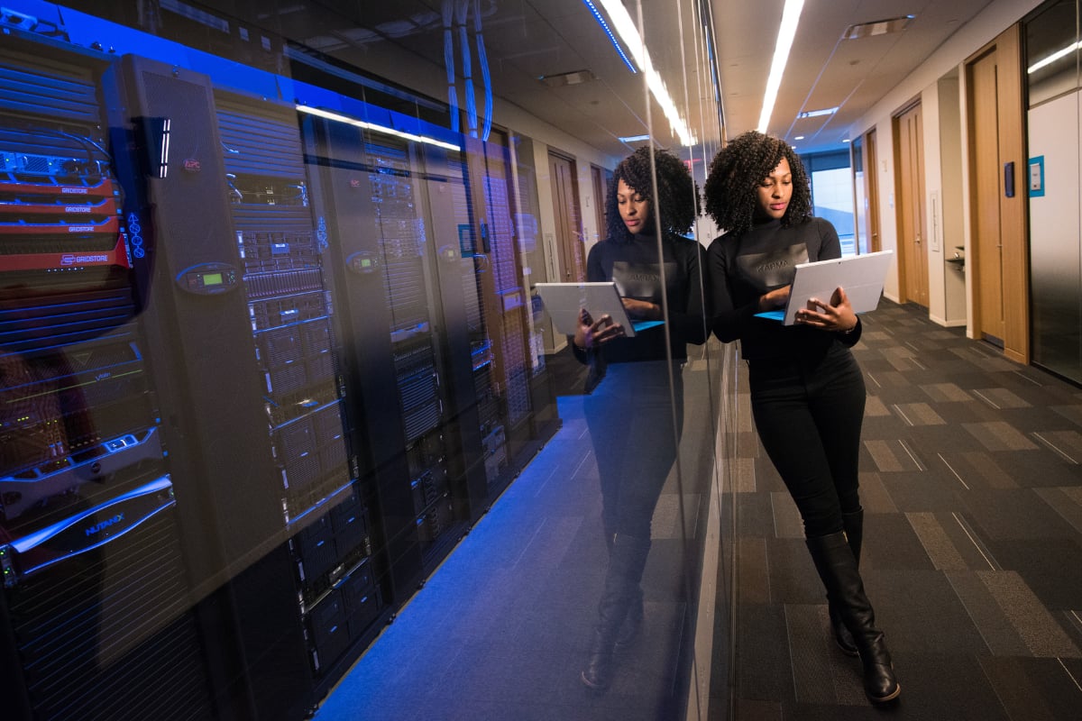 A professional reviews a tablet beside server racks in a modern data center with blue lighting and glass reflections.