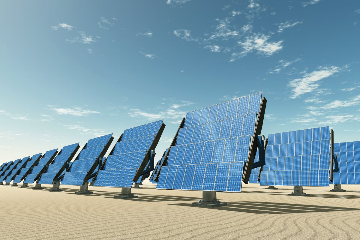Rows of solar panels stand in a sunlit landscape beneath a blue sky with scattered white clouds.