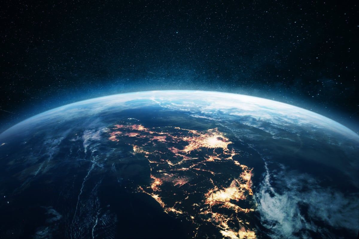 View of Earth from space with glowing city lights, cloud cover, and a star-filled night sky above.