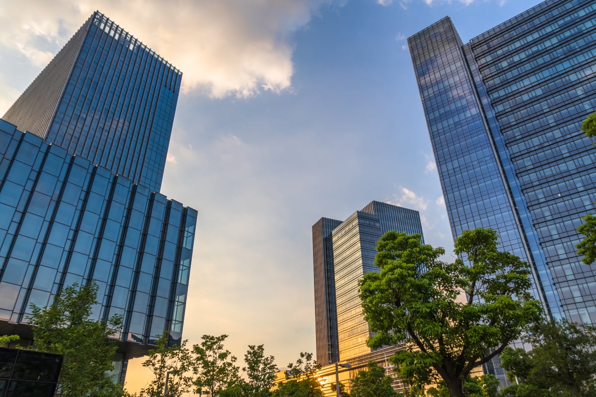 Modern glass skyscrapers surrounded by trees under a blue sky, illustrating sustainable real estate and an urban environment

