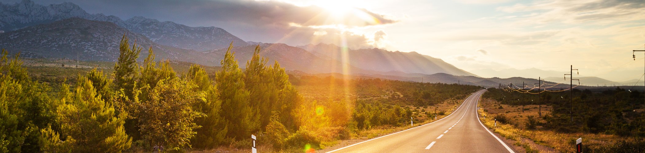 Road through a natural landscape toward mountains at sunset, symbolizing direction, vision and future prospects