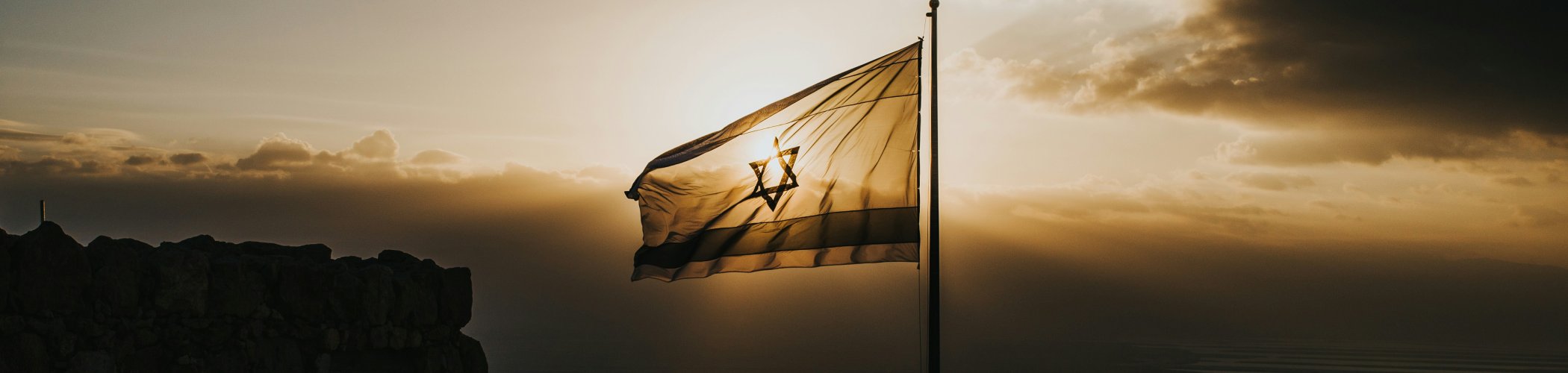 Israeli flag waving at sunset above a rocky landscape, symbolizing the Middle East and geopolitical context