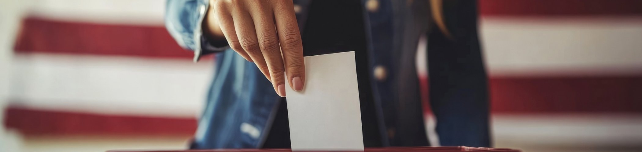 Hand placing a ballot into a voting box in front of a US flag, illustrating elections and democracy in the United States