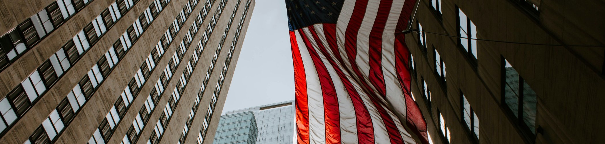 United States flags waving in front of skyscrapers in an urban street, illustrating the American economy and financial center