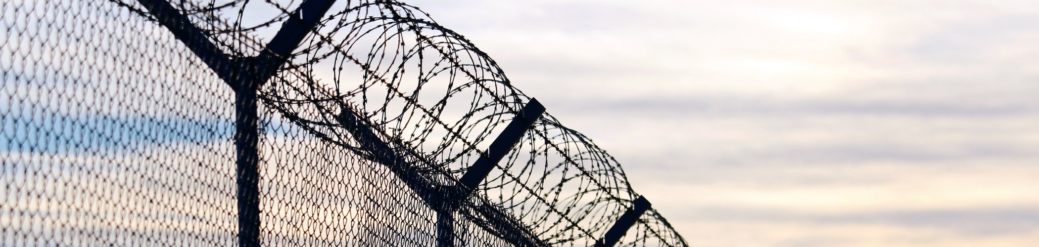 Chain-link fence topped with barbed wire, symbolizing security, protection and access control