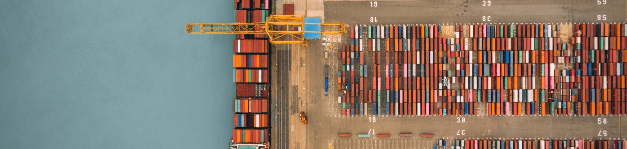 Aerial view of a seaport with a container ship and rows of colorful containers, illustrating global trade and logistics