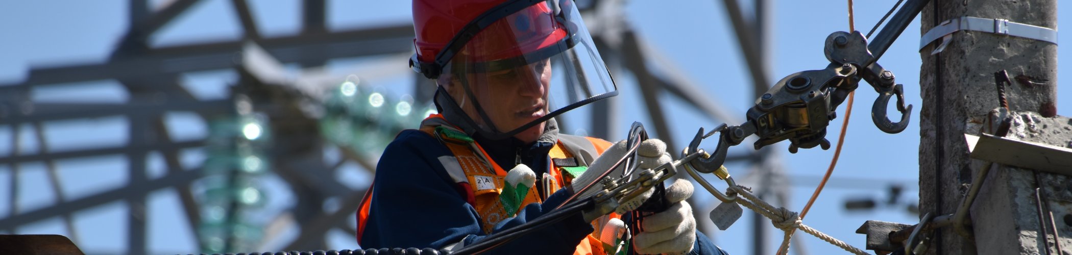 Industrial worker wearing protective equipment while handling cables and equipment on an electrical structure outdoors.

