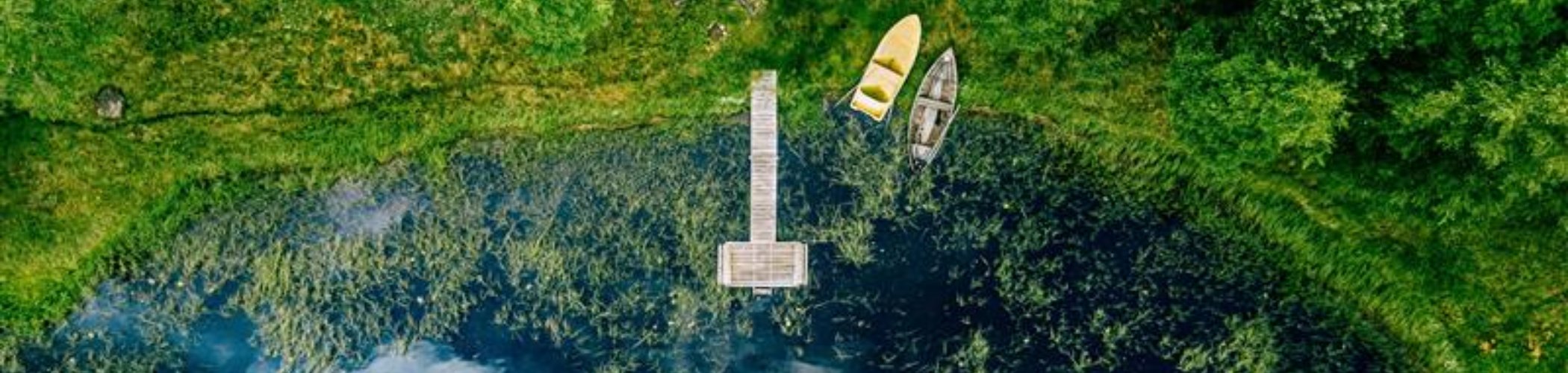 Aerial view of a small lake surrounded by vegetation with a wooden pier and boats, illustrating nature, biodiversity and sustainable landscapes

