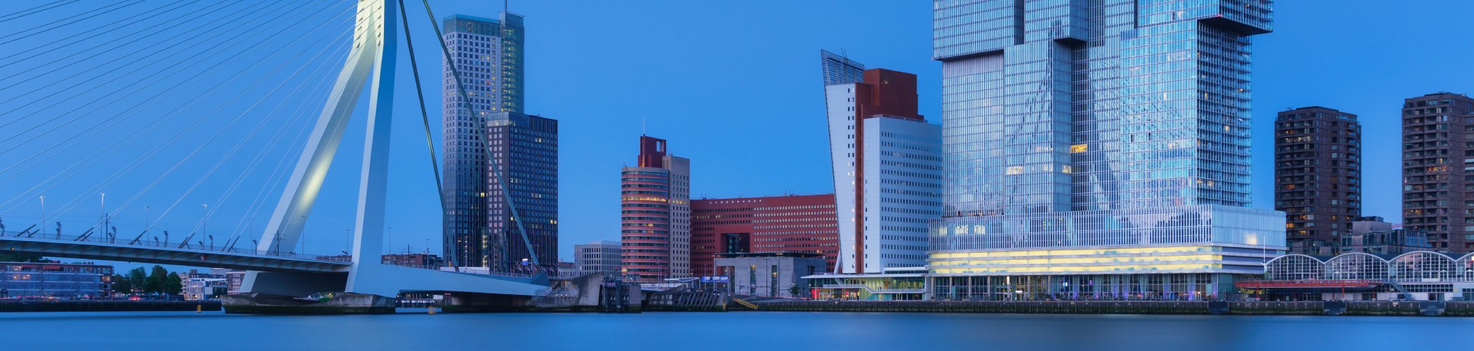 City skyline at dusk featuring modern high‑rise buildings and a cable‑stayed bridge spanning a river.

