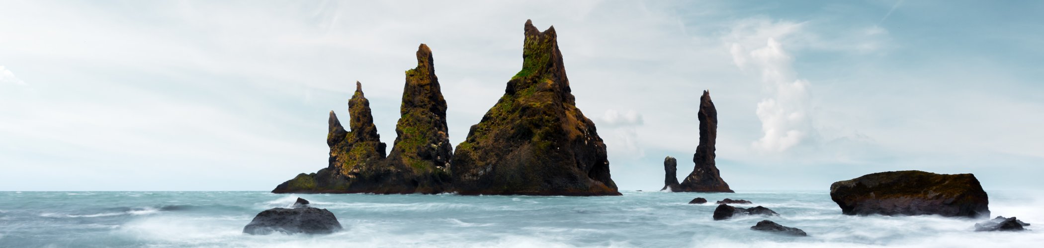 Volcanic rock formations rising from the ocean with waves and cloudy sky, illustrating a wild natural landscape and the power of nature
