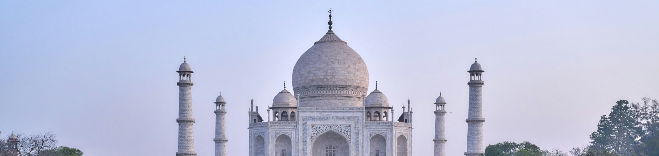 The Taj Mahal stands beyond a long reflecting pool and manicured gardens beneath a hazy morning sky in Agra, India.
