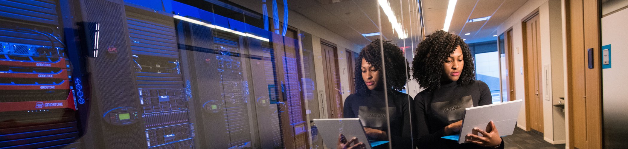 A professional reviews a tablet beside server racks in a modern data center with blue lighting and glass reflections.