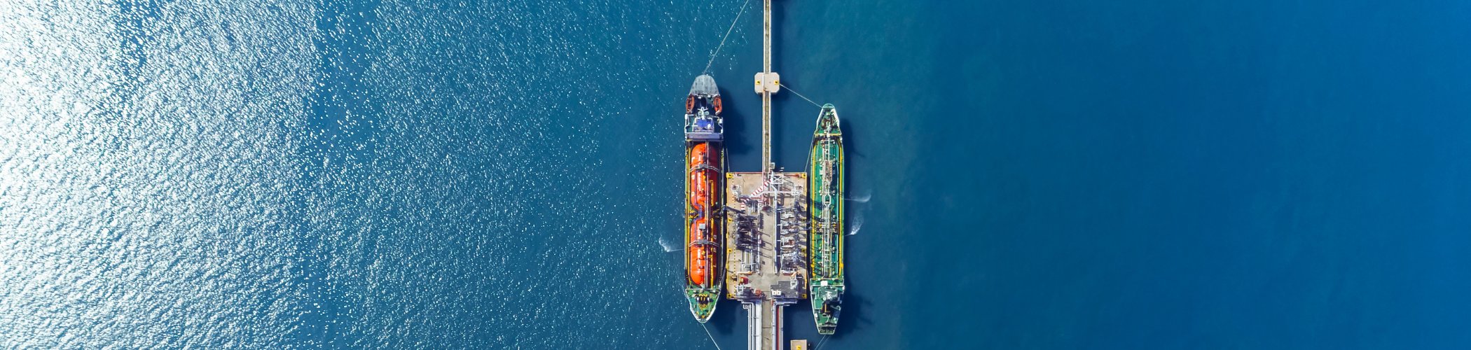Aerial view of a marine terminal with cargo ships docked at a pier surrounded by calm, deep blue water.