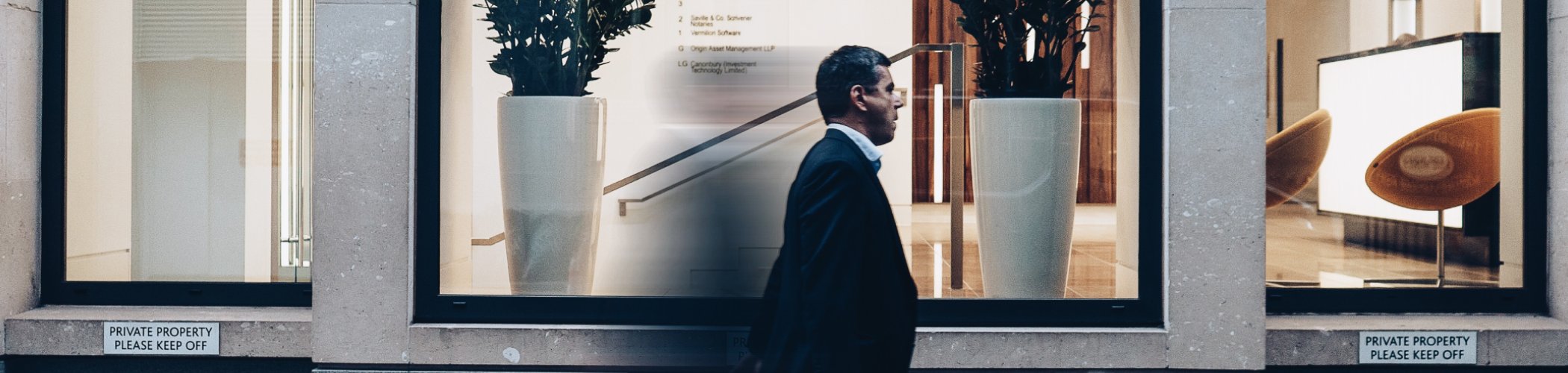 Business professional walking past a modern office building, illustrating financial markets, investment services and corporate activity