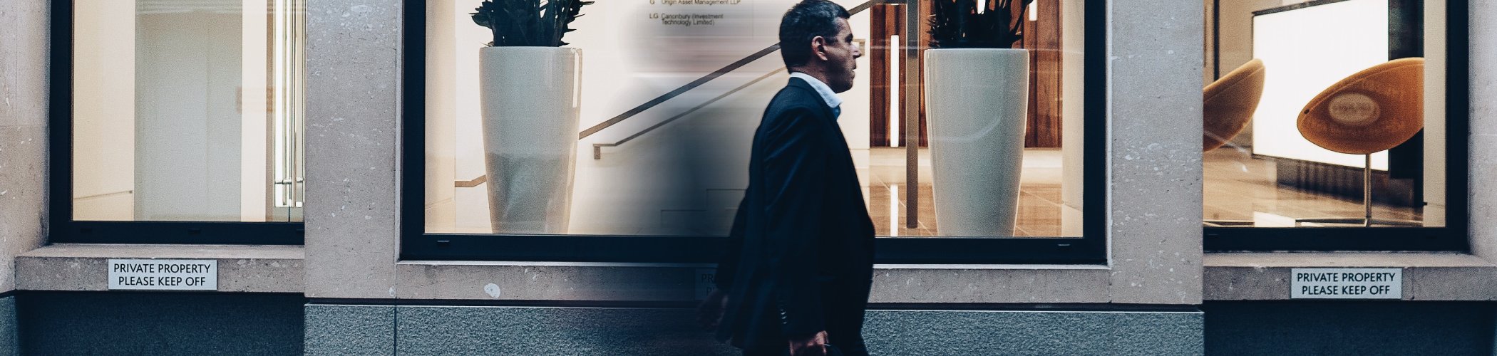 Business professional walking past a modern office building, illustrating financial markets, investment services and corporate activity