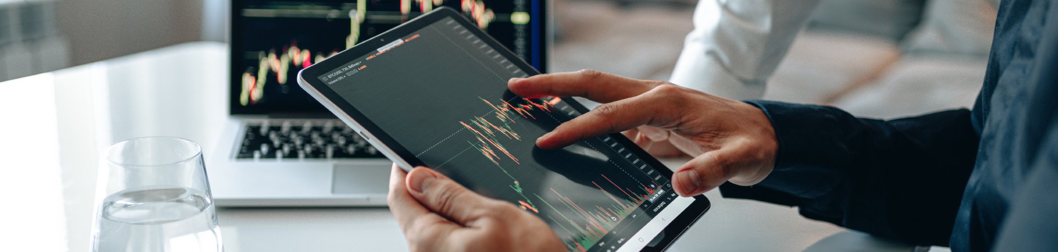 Person reviewing a trading chart on a tablet with a laptop in the background, illustrating financial market analysis
