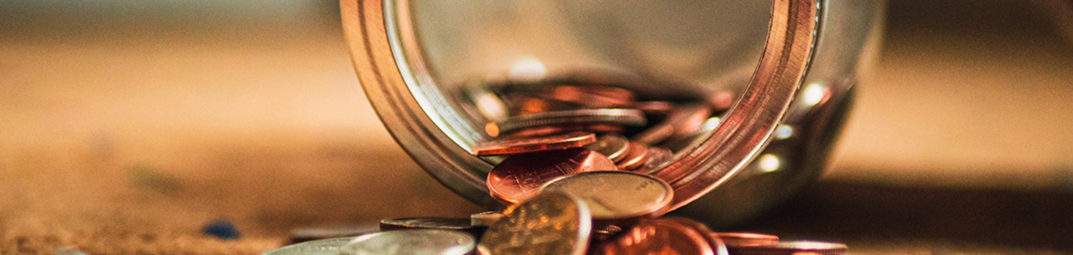Coins spilling out of a glass jar, illustrating savings, personal finance and wealth management
