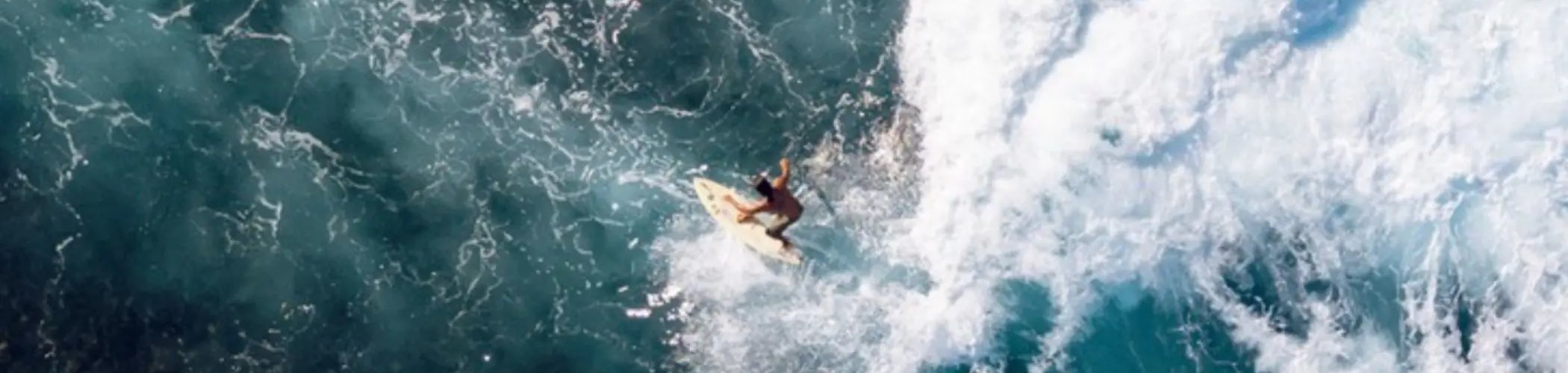 Aerial view of a surfer riding a wave, surrounded by swirling ocean water and white foam.

