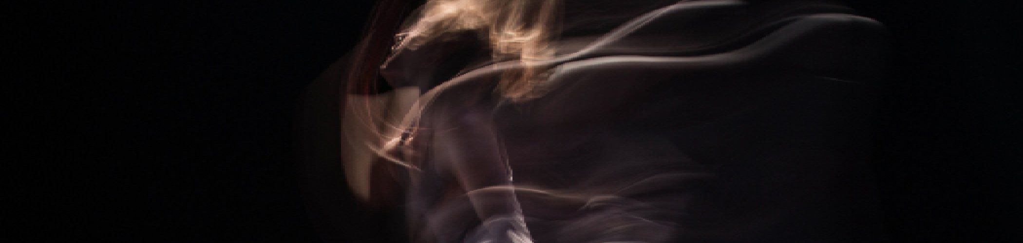 Abstract long‑exposure image showing the blurred motion of a human figure against a dark background, creating flowing light trails.

