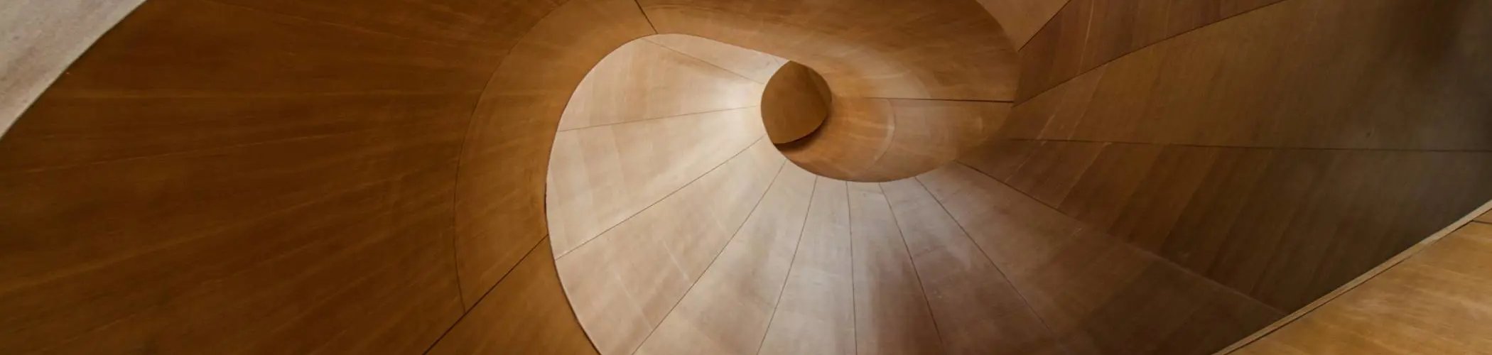 Wooden spiral staircase viewed from above with fluid architectural design, illustrating structure, movement and modern interior architecture