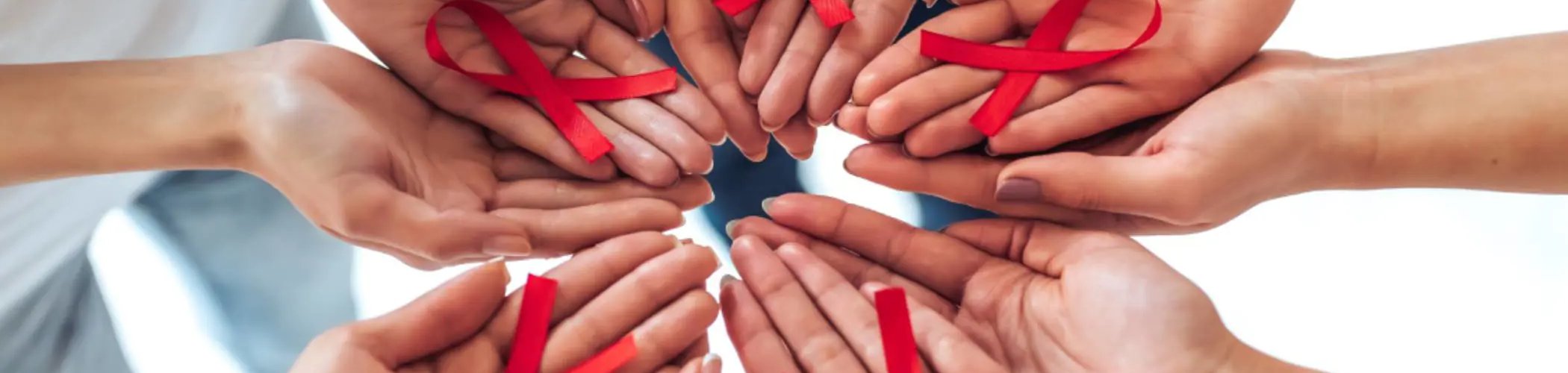 Several open hands arranged in a circle, each holding a red ribbon, symbolizing awareness and support for HIV and AIDS.

