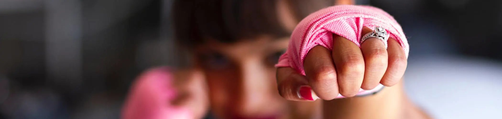 Close‑up of a young person holding two red boxing gloves raised toward the camera, with the face slightly out of focus in the background.


