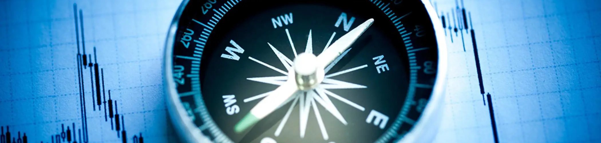 Compass placed on a financial chart with candlesticks, illustrating strategic direction and investment decision-making
