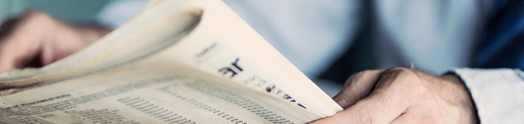 Person flipping through a financial newspaper with market data, illustrating financial news and market analysis

