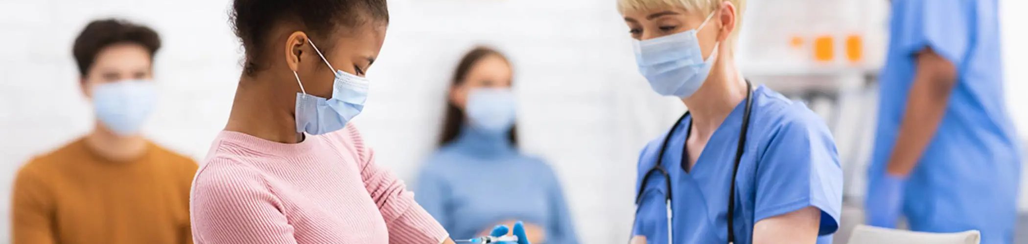 Group of people wearing medical masks in a clinical environment, standing and seated while reviewing documents together